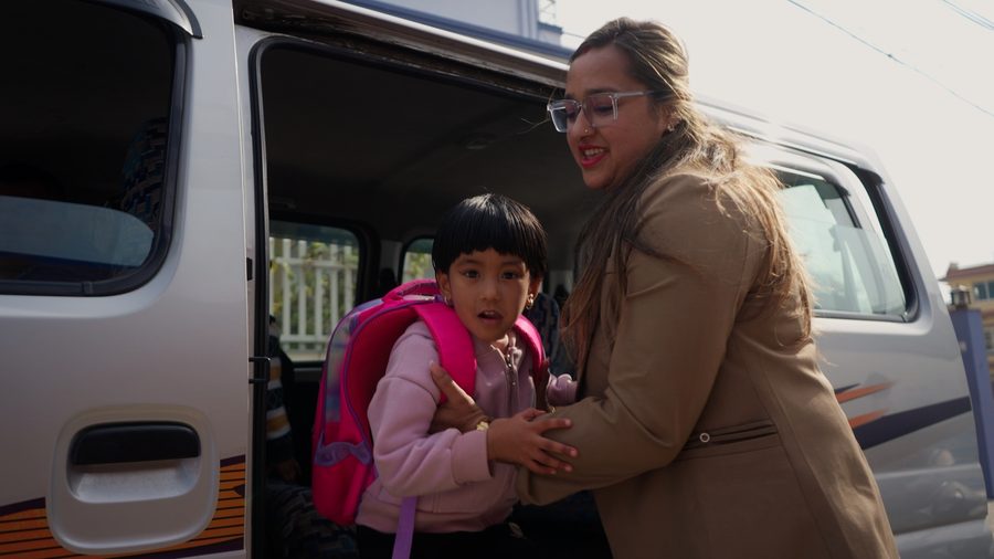 A staff member helping a child down from the school bus
